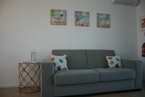 Modern living area at Recantus Comporta with gray sofa, decorative fish pillows, coastal wall art, and side table in Egret