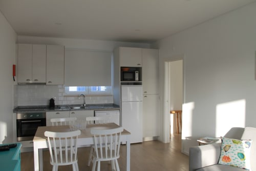 Bright modern kitchen and living area in Egret Apartment at Recantus Comporta, Comporta with white cabinetry and dining table