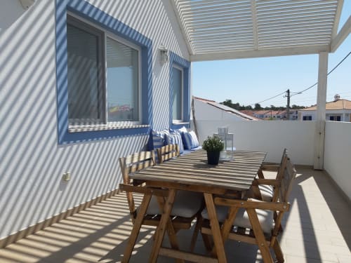 Sunny terrace at Recantus Comporta with wooden dining table, striped pergola, and city views of Comporta, Portugal