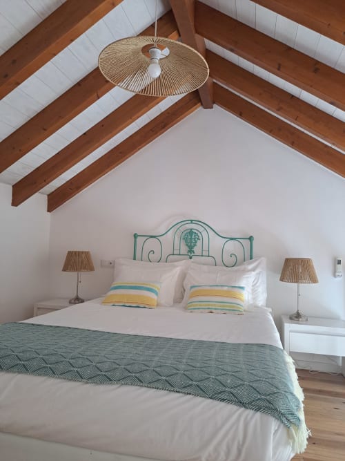 Coastal bedroom at Recantus Comporta with wooden beams, turquoise metal bed, striped pillows, and woven ceiling fan