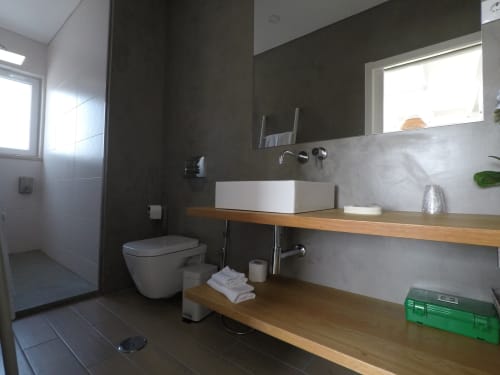 Modern bathroom at Recantus Comporta Stork Apartment in Comporta with floating wooden vanity, white basin sink, and dark tile