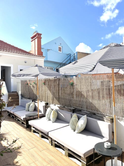 Vila Alexandra hostel rooftop terrace with lounge beds, striped umbrellas, and reed fence in Costa da Caparica