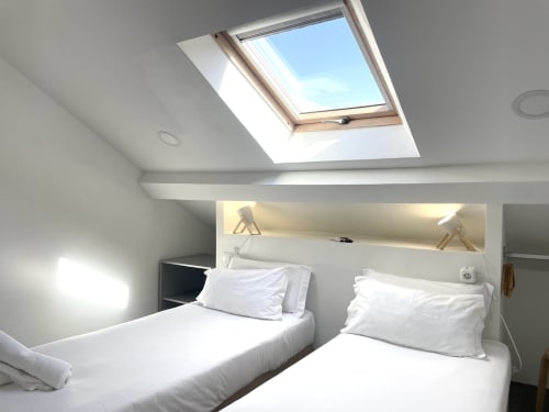 Bright attic bedroom at Vila Alexandra hostel in Costa da Caparica with two beds and skylight window