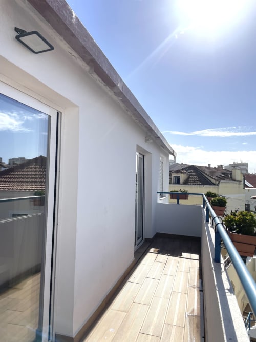Modern rooftop terrace at Vila Alexandra hostel with wooden deck, potted plants, and coastal views in Costa da Caparica