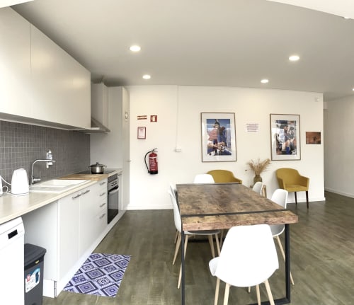 Modern hostel kitchen and dining area at Vila Alexandra in Costa da Caparica with white cabinetry, wooden table, and