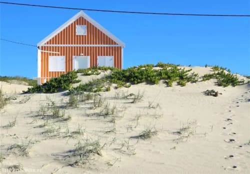 Orange and white beach house at Vila Alexandra hostel in Costa da Caparica, Portugal, set on sandy dunes