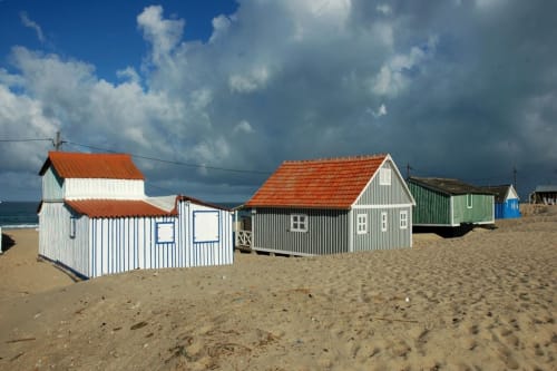 Colorful beach huts at Vila Alexandra hostel in Costa da Caparica, Portugal, lined up on sandy beach