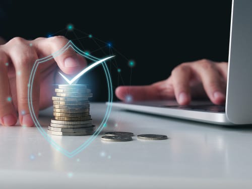 Gestion financière sécurisée pour Home Horizon SBL Limoges : main protégeant des pièces empilées avec icône de bouclier numérique