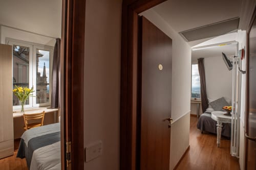 Camera quadrupla all'Hotel Vista Lago a Brunate con porte in legno, scrivania vicino alla finestra con vista sulla città e pavimento in legno duro