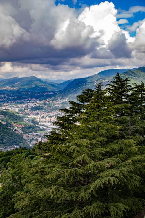 Vista della valle montana dall'Hotel Vista Lago a Brunate, Italia, con pendii boscosi, villaggi distanti e nuvole drammatiche