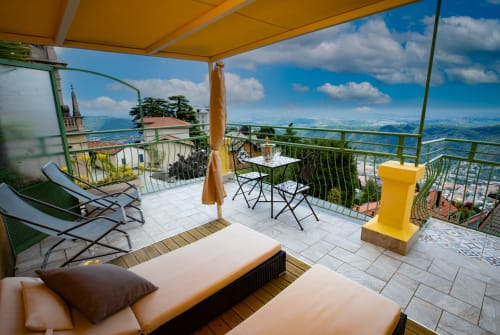 Balcone dell'Hotel Vista Lago con vista sul lago, lettini, ombrellone giallo e montagne di Brunate sullo sfondo