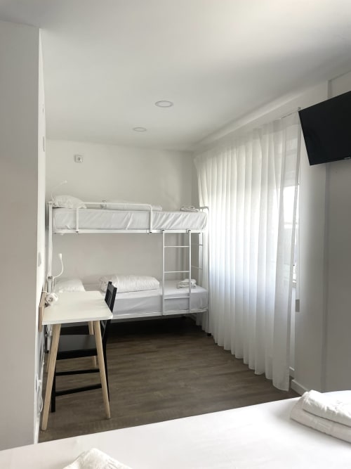 Bright hostel room at Vila Alexandra with white bunk beds, desk, TV, and sheer curtains in Costa da Caparica
