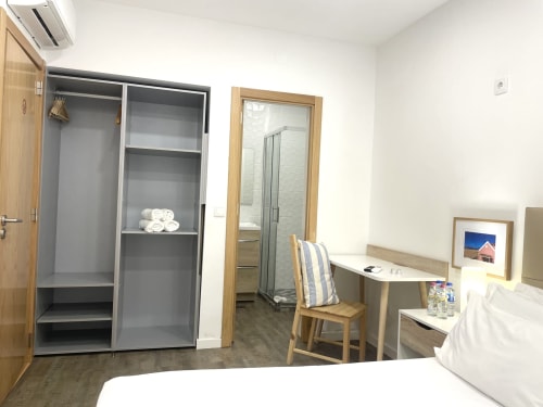 Vila Alexandra hostel room with bed, wooden desk, chair, open closet, and ensuite bathroom in Costa da Caparica