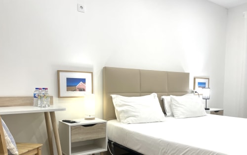 Modern hotel room at Vila Alexandra in Costa da Caparica with queen bed, beige headboard, white bedding, and coastal artwork