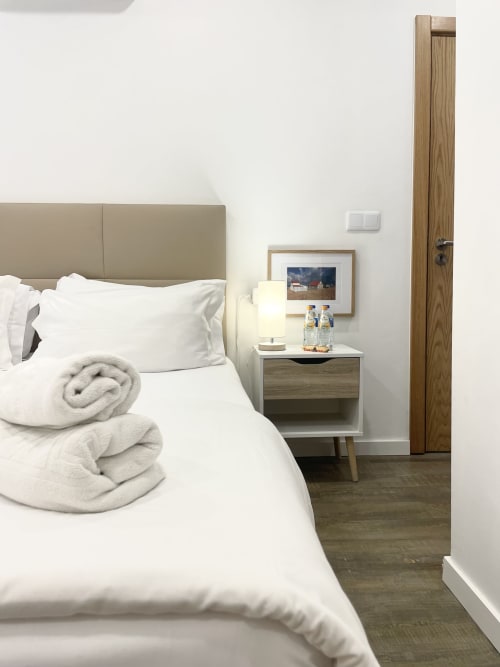 Modern bedroom at Vila Alexandra hostel in Costa da Caparica with white bedding, beige headboard, and wooden door