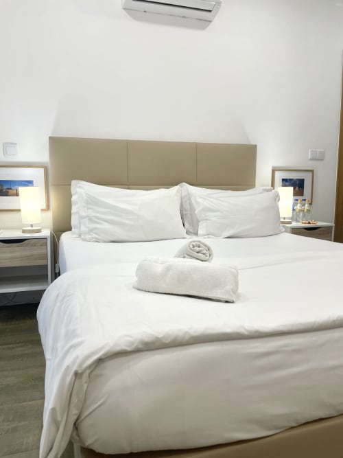 Clean white bedding with rolled towels in Room 5 at Vila Alexandra hostel, Costa da Caparica, Portugal