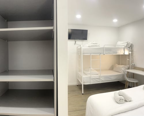 Hostel Room 5 at Vila Alexandra in Costa da Caparica with bunk beds, wall-mounted TV, desk, and open closet storage