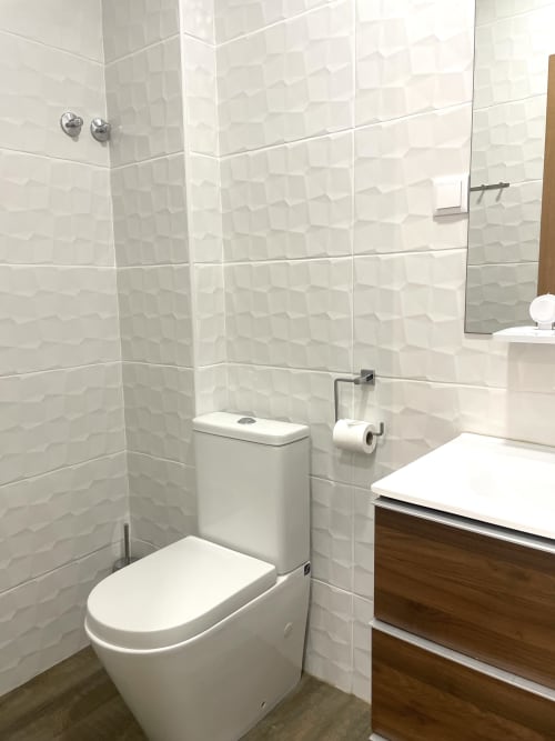 Modern bathroom at Vila Alexandra hostel in Costa da Caparica with white textured tiles, toilet, sink, and wood vanity