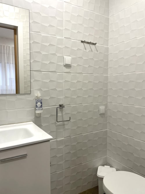 Modern bathroom with textured white tile walls, glass shower enclosure, white sink vanity, and toilet at Vila Alexandra
