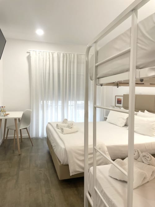 Modern hostel room at Vila Alexandra, Costa da Caparica with white bunk beds, desk, and natural light from curtained windows