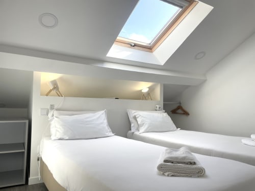 Bright attic bedroom at Vila Alexandra hostel with twin beds, skylight, and modern amenities in Costa da Caparica