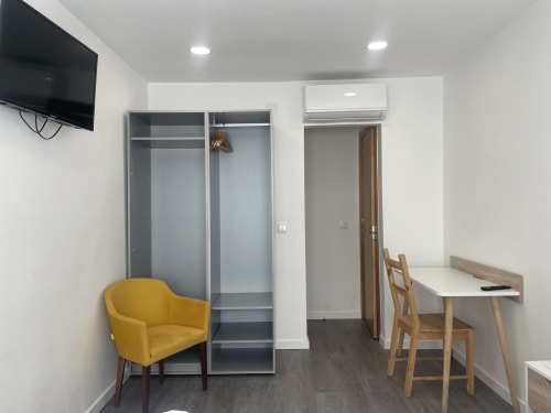 Modern hostel room at Vila Alexandra in Costa da Caparica with yellow chair, desk, wardrobe, TV, and air conditioning