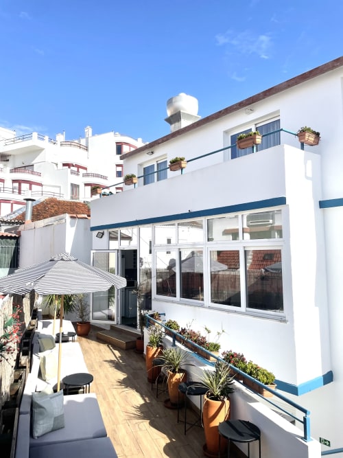 Vila Alexandra hostel terrace in Costa da Caparica with wooden deck, potted plants, striped umbrella, and white modern