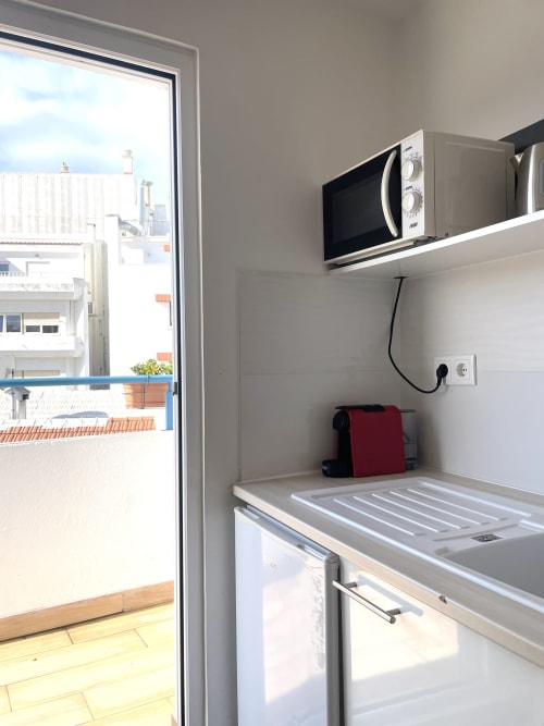 Compact kitchenette in Vila Alexandra hostel room with microwave, stovetop, refrigerator, and city view balcony access in