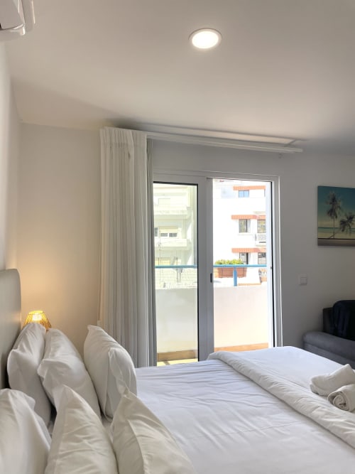 Modern bedroom at Vila Alexandra hostel in Costa da Caparica with white bedding, balcony door, city view, and contemporary