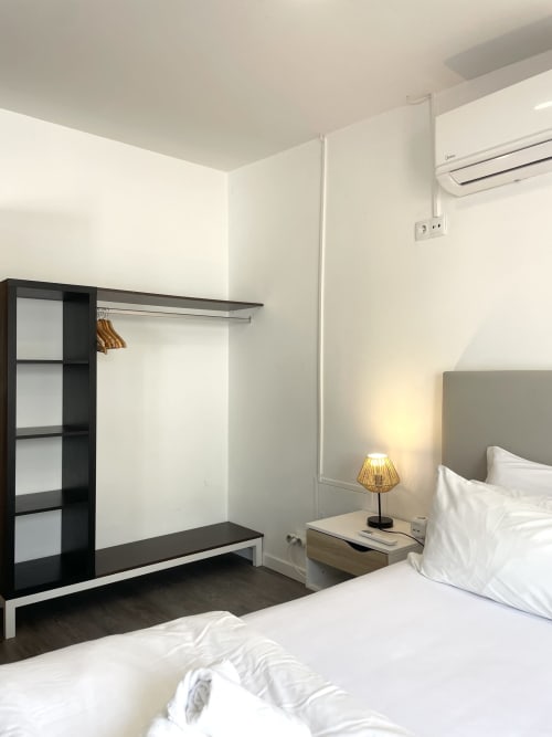 Modern bedroom at Vila Alexandra hostel in Costa da Caparica with bed, nightstand lamp, black wardrobe, and air conditioning