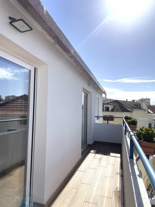 Sunny balcony at Vila Alexandra hostel in Costa da Caparica with wooden deck, potted plants, and city rooftop views