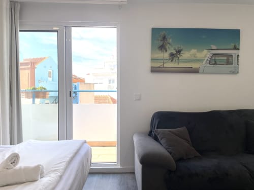 Vila Alexandra hostel room with bed, black sofa, balcony overlooking colorful Costa da Caparica buildings and ocean view