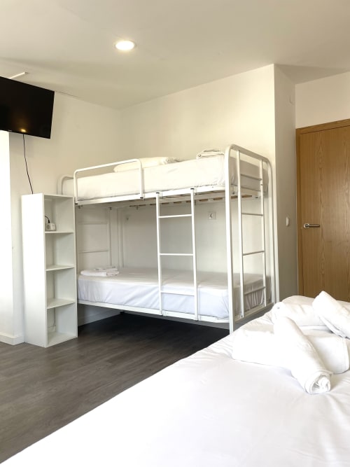 Modern hostel bedroom at Vila Alexandra in Costa da Caparica with bunk beds, single bed, TV, and wooden storage
