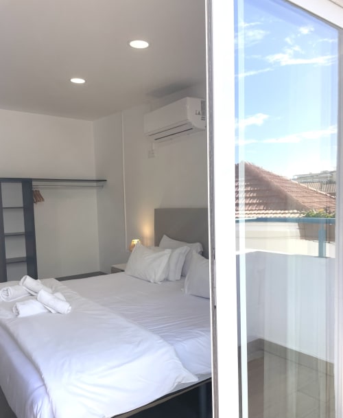 Bright modern bedroom at Vila Alexandra hostel in Costa da Caparica with white bedding, air conditioning, and balcony