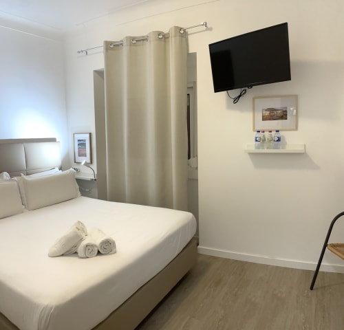 Modern hostel room at Vila Alexandra in Costa da Caparica with bed, TV, shower curtain divider, and amenities shelf