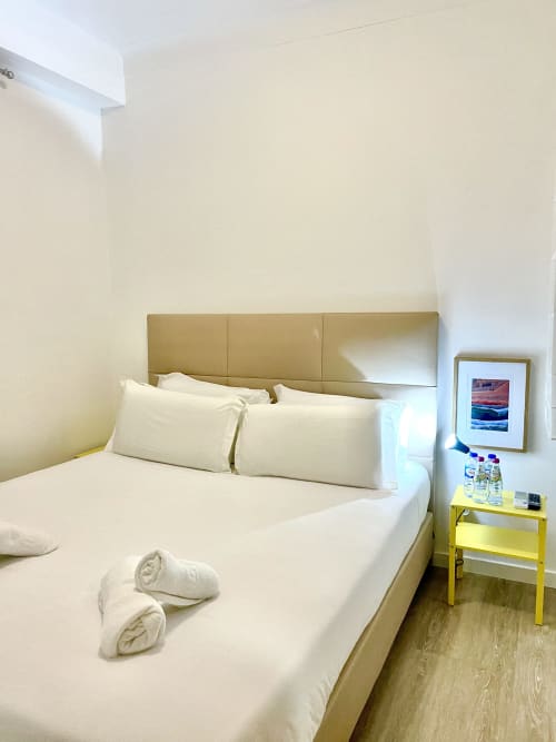 Vila Alexandra hostel room B4 with white bedding, padded headboard, yellow nightstand, and framed beach artwork in Costa da