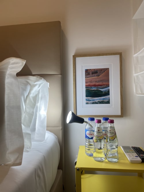 Cozy hostel room at Vila Alexandra in Costa da Caparica with bed, yellow nightstand, water bottles, and coastal artwork