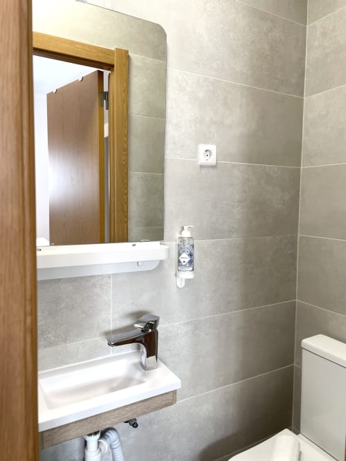 Modern bathroom at Vila Alexandra hostel in Costa da Caparica with white sink, wooden mirror frame, and gray tiled walls