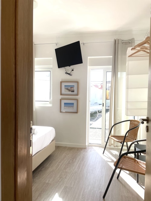 Modern hostel room at Vila Alexandra, Costa da Caparica with bed, TV, balcony access, and beach-themed décor