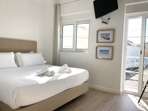 Bright bedroom at Vila Alexandra hostel in Costa da Caparica with bed, TV, balcony doors, and beach artwork