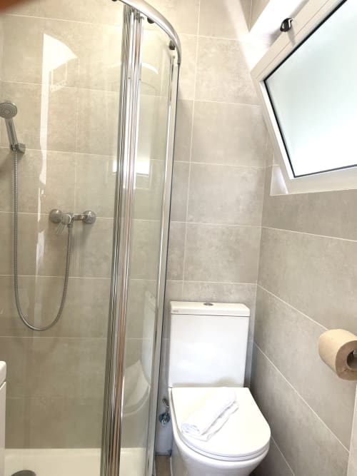 Modern bathroom with shower enclosure, white toilet, and beige tile walls at Vila Alexandra hostel, Costa da Caparica