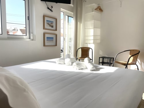 Bright hostel bedroom at Vila Alexandra, Costa da Caparica with white bed, wicker chairs, balcony access and city views