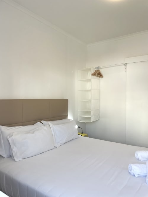 Clean modern bedroom at Vila Alexandra hostel in Costa da Caparica with white bedding, taupe headboard, and built-in storage