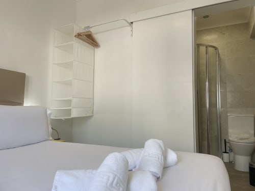 Hostel room bed with white linens and bathroom at Vila Alexandra, Costa da Caparica