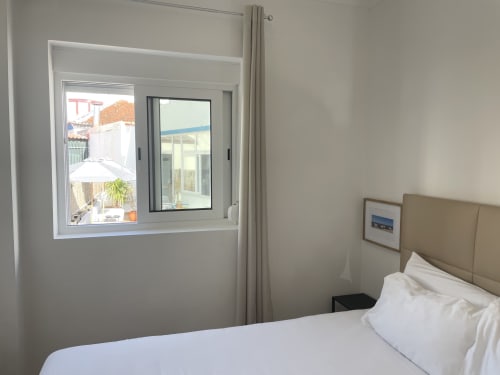 Modern bedroom at Vila Alexandra hostel in Costa da Caparica with white bedding, beige headboard, and window overlooking