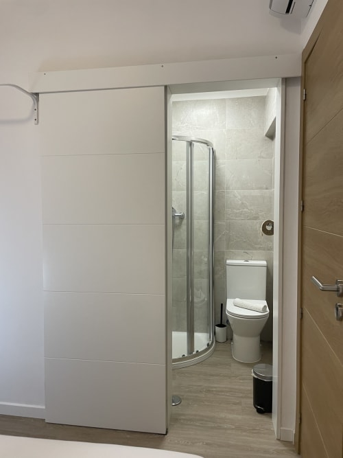Modern ensuite bathroom with curved glass shower enclosure at Vila Alexandra hostel, Costa da Caparica