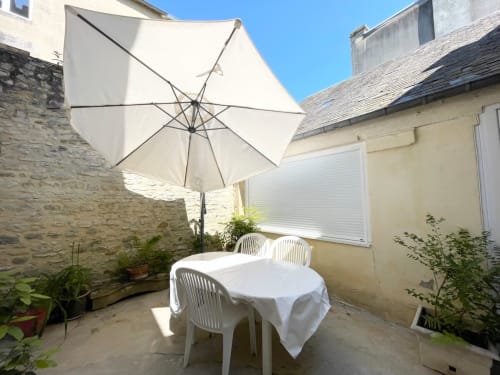 Sunny courtyard patio at Le 58 Bayeux with white umbrella, dining table, and stone walls in Bayeux, France