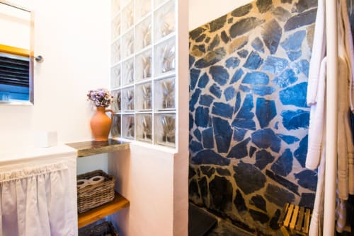 Banheiro moderno em Casas de Juromenha com chuveiro de azulejos geométricos azuis, vaso laranja e iluminação natural abundante