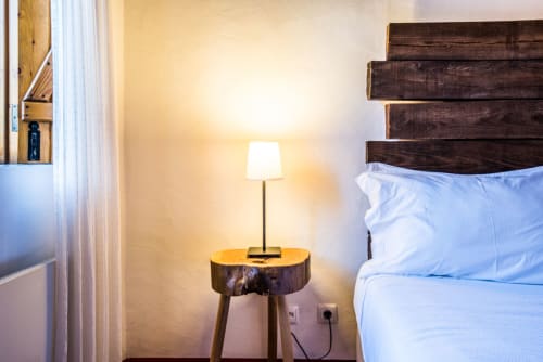 Quarto aconchegante em Casas de Juromenha com cabeceira de madeira, roupa de cama azul e luminária morna em criado rústico