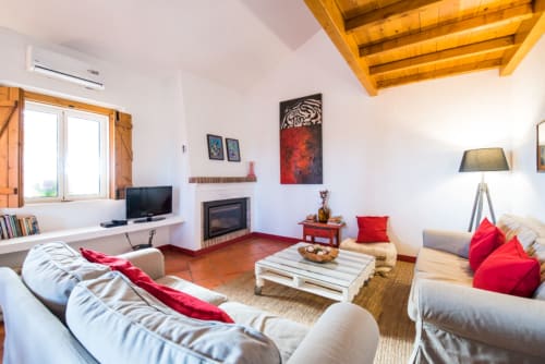 Sala de estar luminosa em Casas de Juromenha com vigas de madeira, lareira, assentos confortáveis e almofadas vermelhas